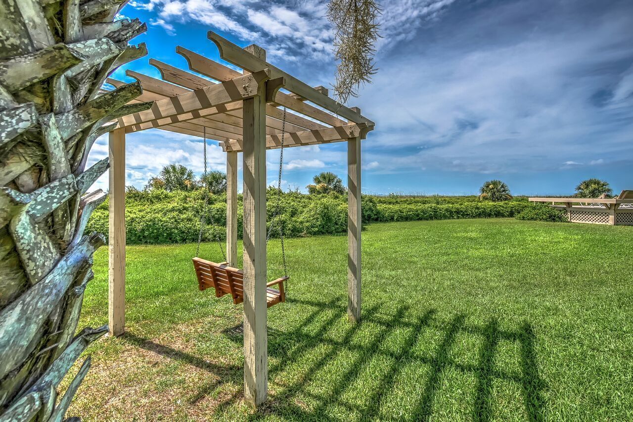 Een houten pergola met een schommelset in een verzorgd gazon.