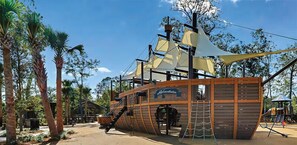 Explore the pirate ship play structure, featuring a mast, crow's nest, and interactive climbing elements.