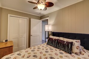 Ein Schlafzimmer mit einem Bett, einem Deckenventilator, einem Nachttisch und einer Tür.