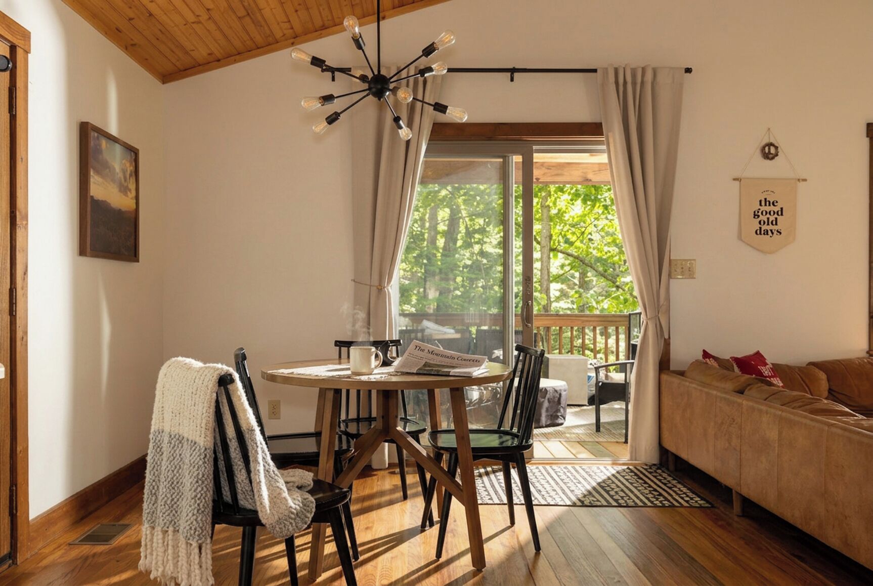Une pièce chaleureuse avec un plafond en bois, une table ronde entourée de chaises, un canapé et une vue sur la verdure à l’extérieur.