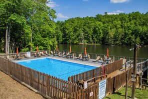 Ein rechteckiger Pool mit Holzterrasse, umgeben von einem Holenzaun, mit einem See im Hintergrund.