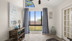 A room with a large window, a ceiling fan, a wooden bench, a lamp, and a wall with a motivational quote.