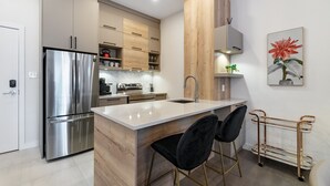 Une cuisine moderne dotée d’un réfrigérateur en acier inoxydable, de meubles en bois, d’un îlot en marbre et d’une table basse en verre.