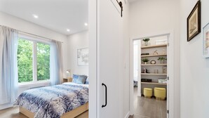 Une chambre à coucher avec un lit, une fenêtre avec des rideaux, une table de chevet et une commode.