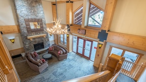 A spacious living area with a stone fireplace, a chandelier, and a large window overlooking a deck. - Spectacular views, just steps from Super Bee, Vaulted Ceilings! Free WiFi (copper mountain)