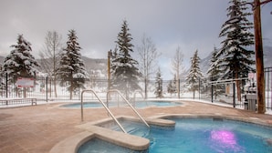 A pool area with a hot tub, surrounded by snow-covered trees and a mountainous backdrop. - Spectacular views, just steps from Super Bee, Vaulted Ceilings! Free WiFi (copper mountain)