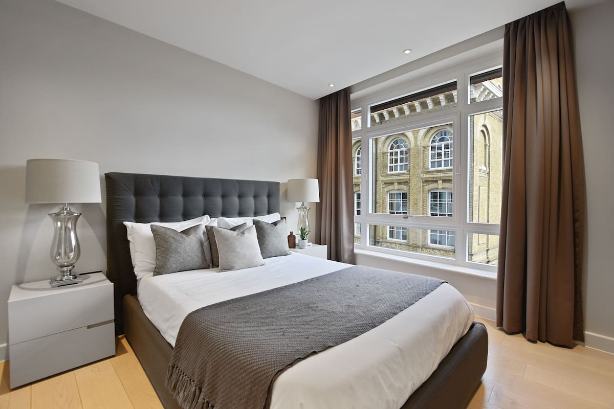 Un dormitorio moderno con una cama grande, dos mesitas de noche y vistas a un edificio histórico a través de la ventana.