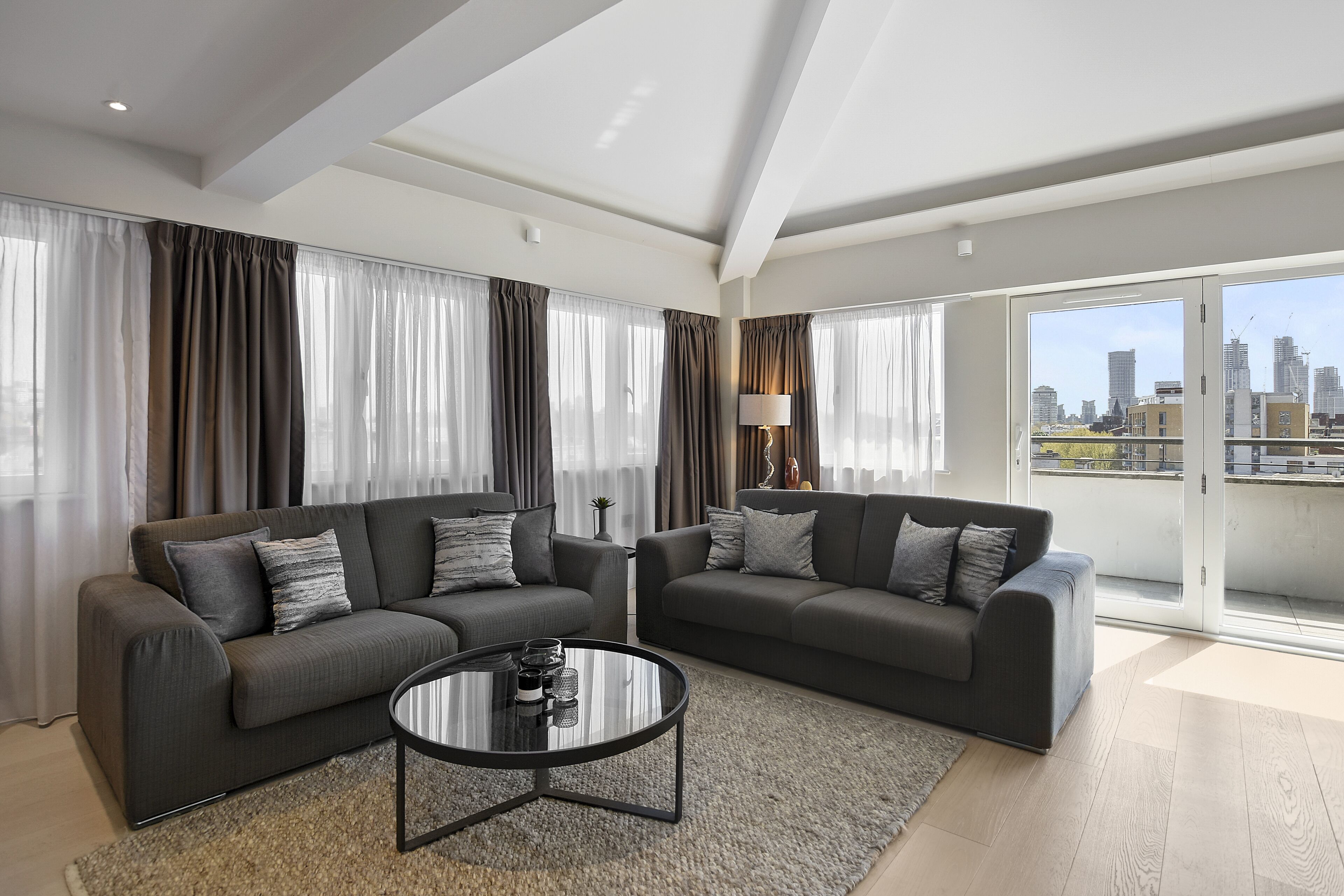 A modern living room with two grey sofas, a round coffee table, and a view of the city through large windows.
