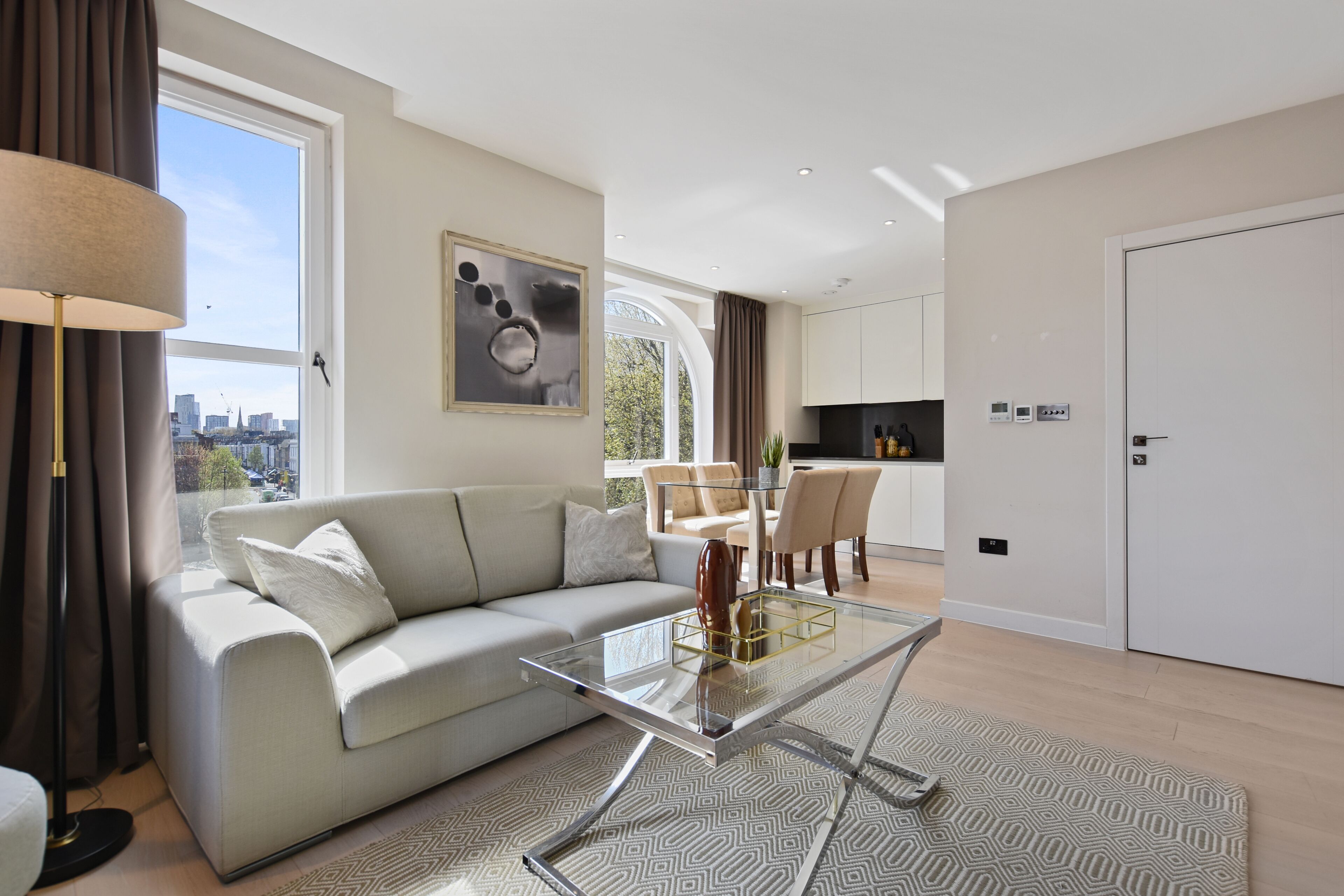 A modern living room with a glass coffee table, a sofa, and a dining area with chairs.