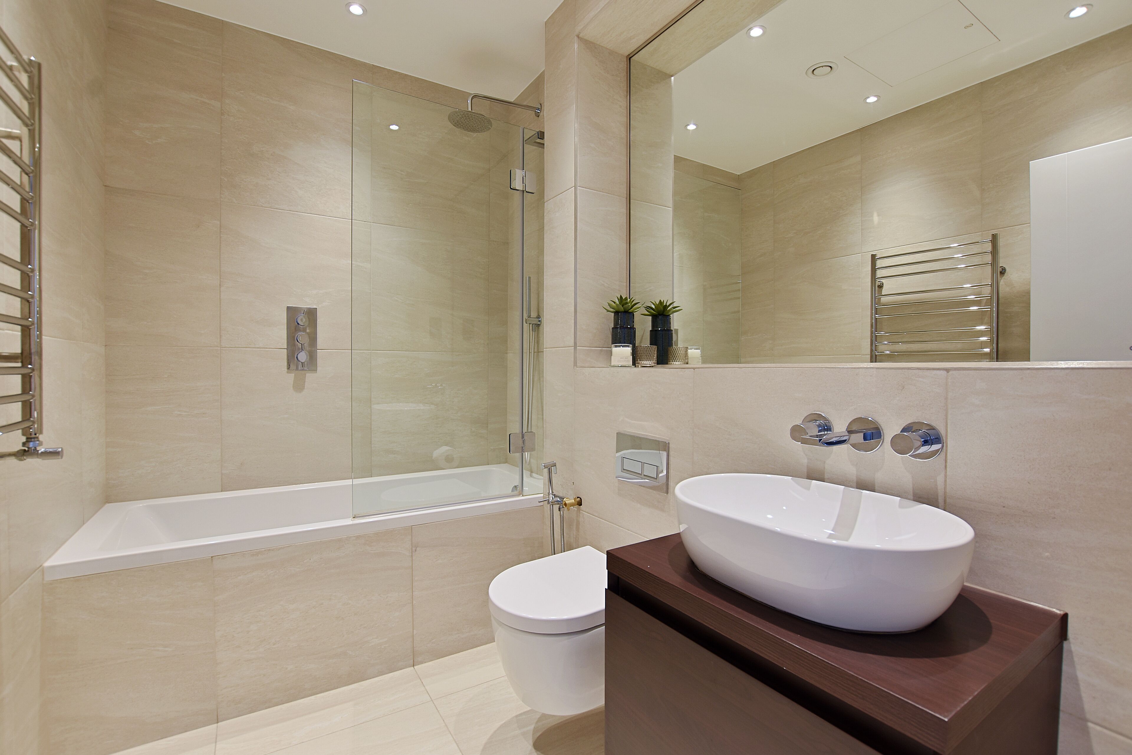 Ein modernes Badezimmer mit einer gläsernen Duschkabine, einer weißen Badewanne und einem großen Spiegel über einem hölzernen Waschtisch mit einem weißen Waschbecken.