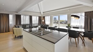 A modern living room with a central island, a dining area, and large windows offering city views.