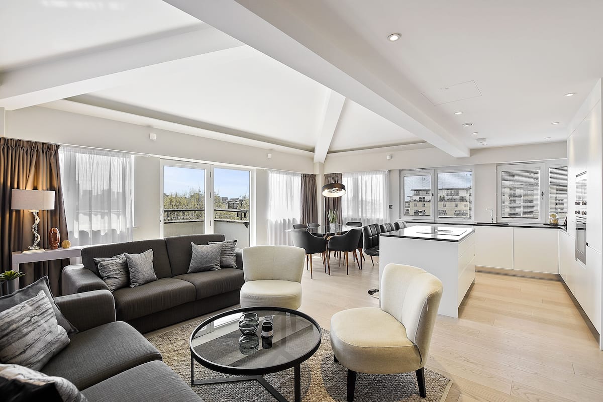 Una sala de estar moderna con un sofá, sillones, una mesa de centro y una zona de cocina con un comedor.