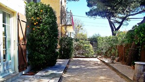A narrow paved pathway flanked by greenery and a building with a window and a door. - T3 2nd floor of the villa of the sea (Hyères)