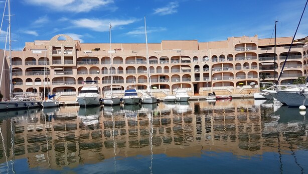 A marina with multiple boats docked in front of a multi-story building with balconies. - T3 2nd floor of the villa of the sea (Hyères)