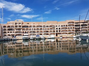 A marina with multiple boats docked in front of a multi-story building with balconies. - T3 2nd floor of the villa of the sea (Hyères)
