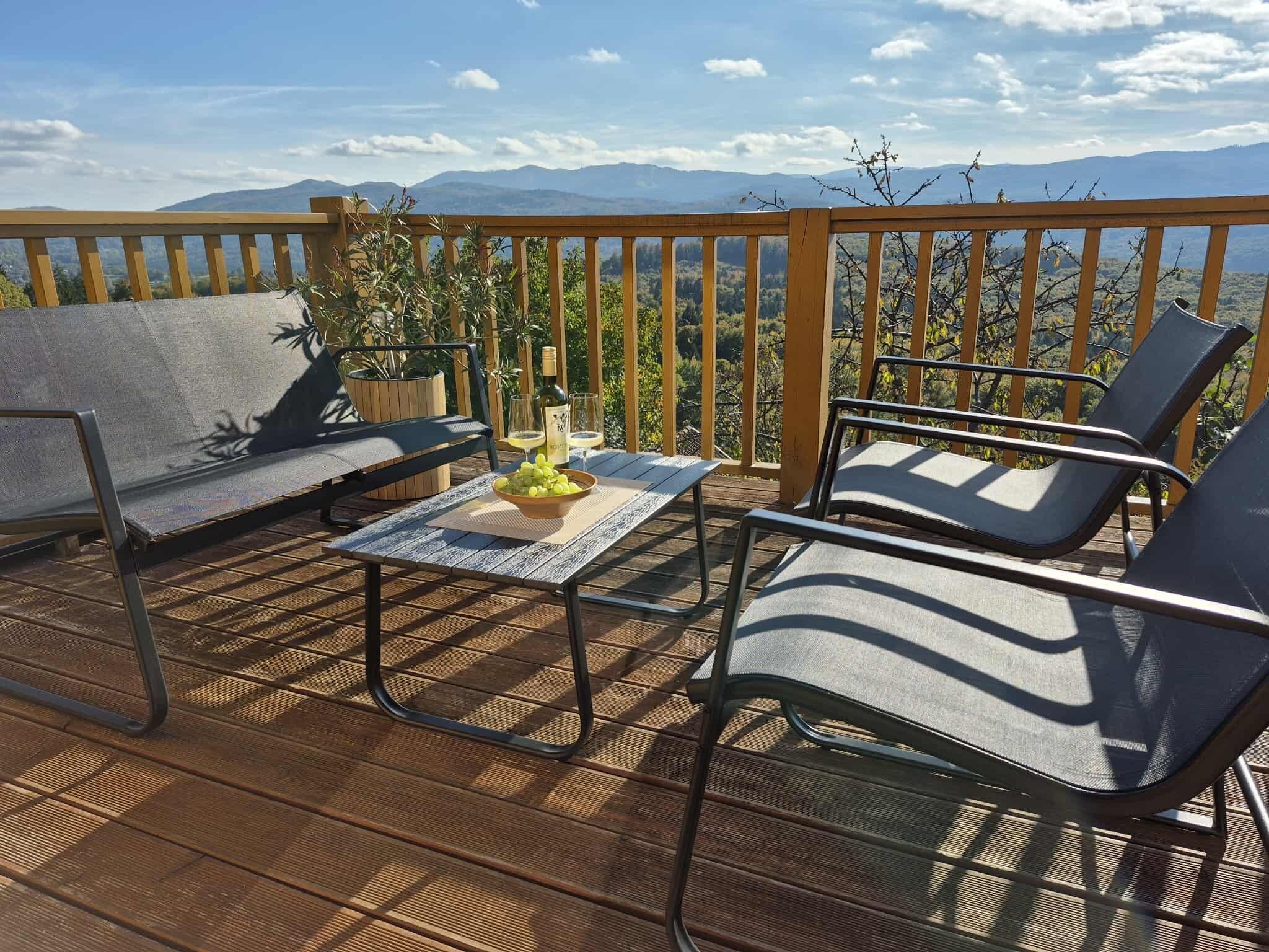 A wooden deck with two lounge chairs and a table, a bottle of wine, and a bowl of grapes.