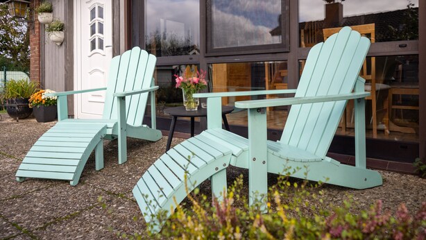 Two Adirondack chairs outside a house with a large window, a door, and a small table with a vase of flowers. - House (Simonsberg)