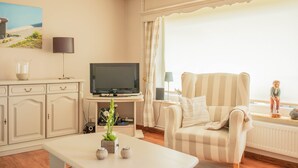 A living room with a television, a sofa, a coffee table, and a window with curtains. - House (Simonsberg)