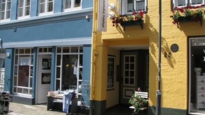 A building with a yellow facade, a sign reading "Askleidestrasse," and a window display with flowers. - House (Simonsberg)