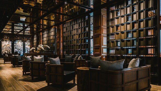 A library with rows of bookshelves, wooden flooring, and comfortable seating areas. - Payaa Hotel (Pattaya)