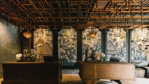 A room with a high ceiling, wooden beams, and a large mural on the back wall. There are two wooden desks with decorative items on them. - Payaa Hotel (Pattaya)