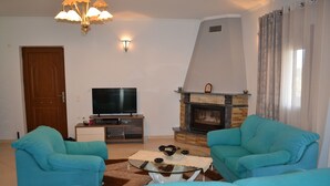 Un salon avec deux canapés bleus, un téléviseur, une cheminée et un lustre.