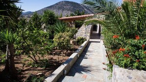 A pathway leading to a stone building with a tiled roof, surrounded by lush greenery and a mountainous backdrop. - Feels Like Your Home at Ermioni (Ermionida)