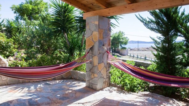 A hammock tied between stone pillars on a stone patio with a view of trees and a body of water. - Feels Like Your Home at Ermioni (Ermionida)