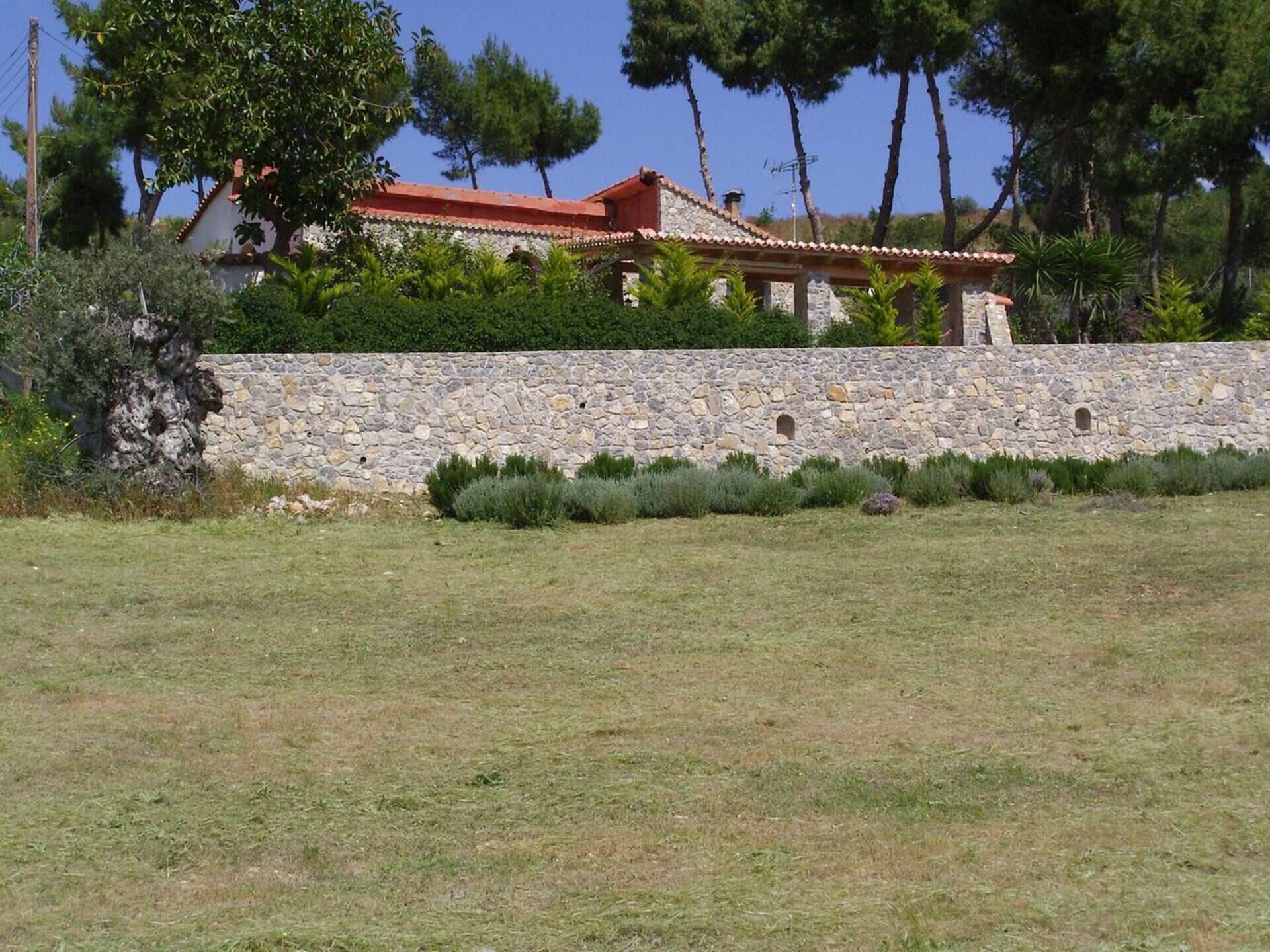 Un mur de pierre avec un petit jardin devant un bâtiment dont le toit est rouge.