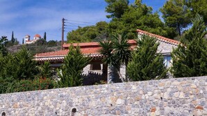 A stone wall with a stone building behind it, featuring a red-tiled roof and surrounded by trees. - Feels Like Your Home at Ermioni (Ermionida)