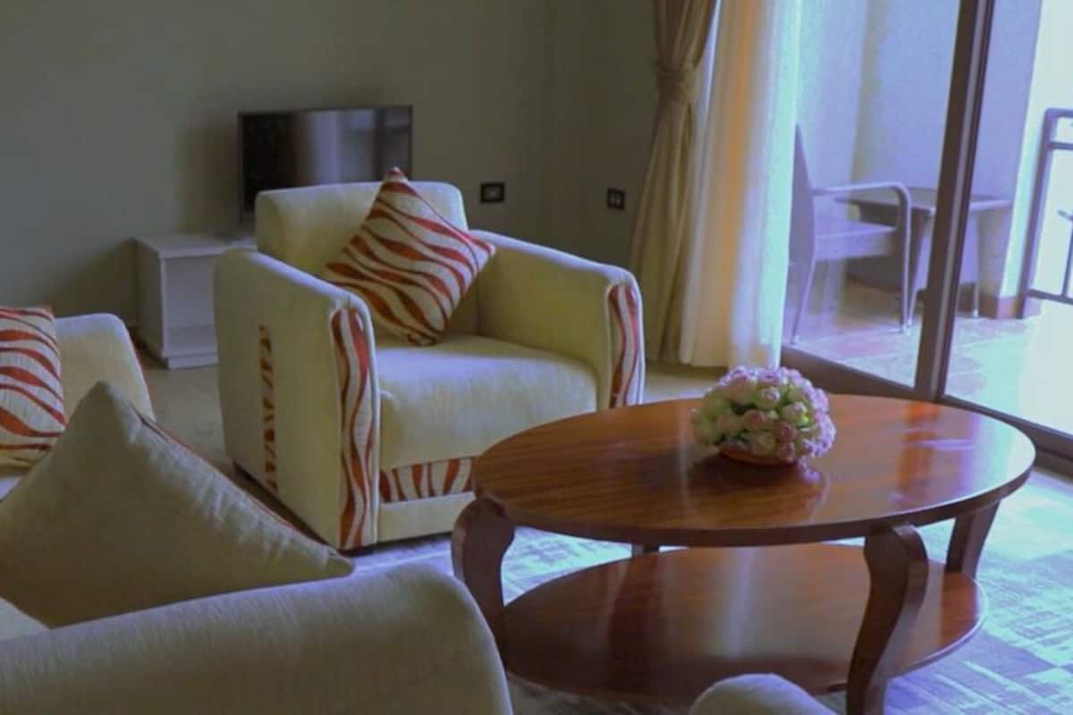 Une chambre d’hôtel avec un canapé, des fauteuils, une table ronde en bois et un téléviseur.
