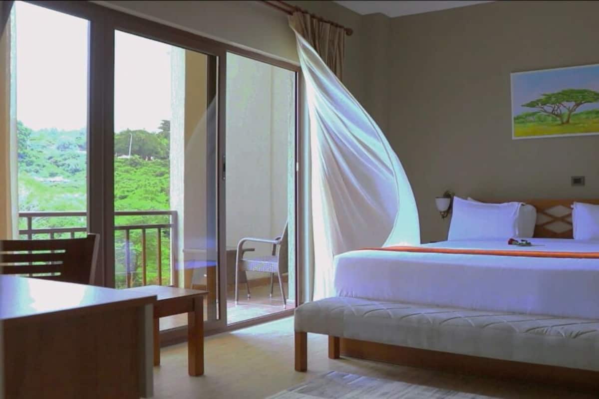 Une chambre avec un lit, une chaise, une table et une vue sur la verdure par la fenêtre.