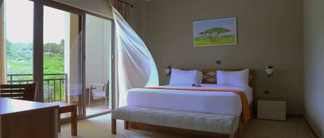 A bedroom with a bed, a chair, a table, and a view of greenery through the window.
