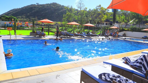 A swimming pool with lounge chairs and umbrellas, surrounded by greenery and a hilly landscape. - Haile Resort Adama (Adama)