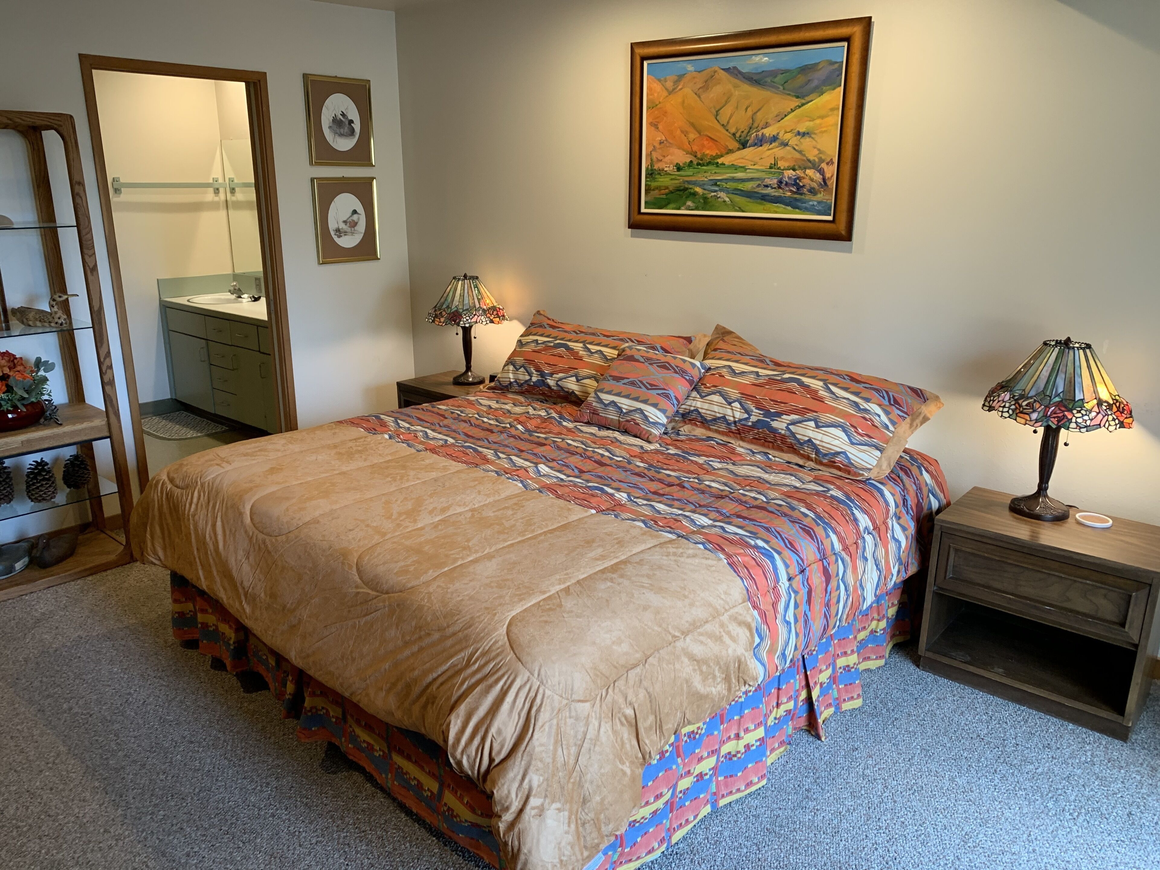 A bedroom with a large bed, two bedside tables with lamps, a mirror, and framed artwork on the wall.