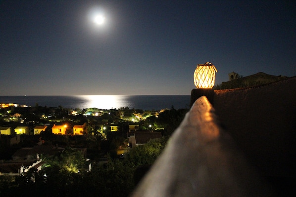 A night view of a coastal town with a prominent lighthouse and a view of the sea.