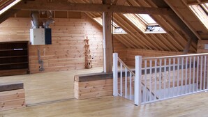 Une pièce mansardée en bois, dotée de fenêtres de toit, d’un escalier en bois et d’une rambarde blanche.