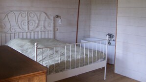 Une chambre avec un lit simple, dotée d’une tête de lit en métal blanche, d’une table de chevet et d’un luminaire suspendu.