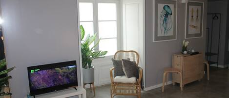 A living room with a flat-screen TV, a wicker chair, a wooden cabinet, and a potted plant.