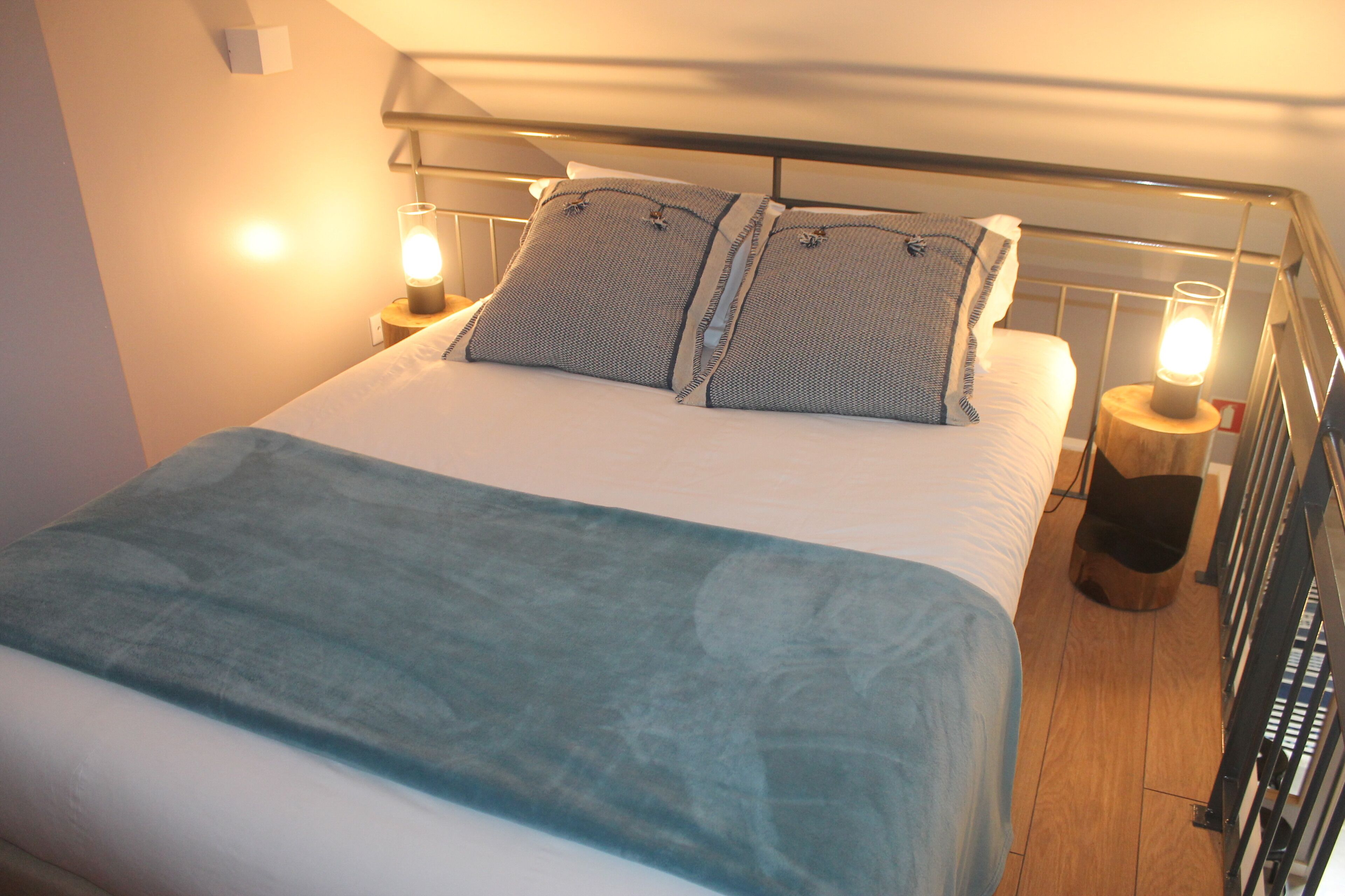 A neatly made bed with a blue blanket, two pillows, and two bedside lamps.