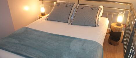 A neatly made bed with a blue blanket, two pillows, and two bedside lamps.