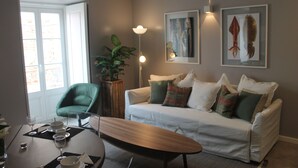Una sala de estar con sofá blanco, una silla verde, mesa de comedor y obras de arte en la pared.