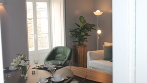 Un comedor con una mesa dispuesta para cuatro personas, una silla verde, un sofá blanco y una planta en maceta.