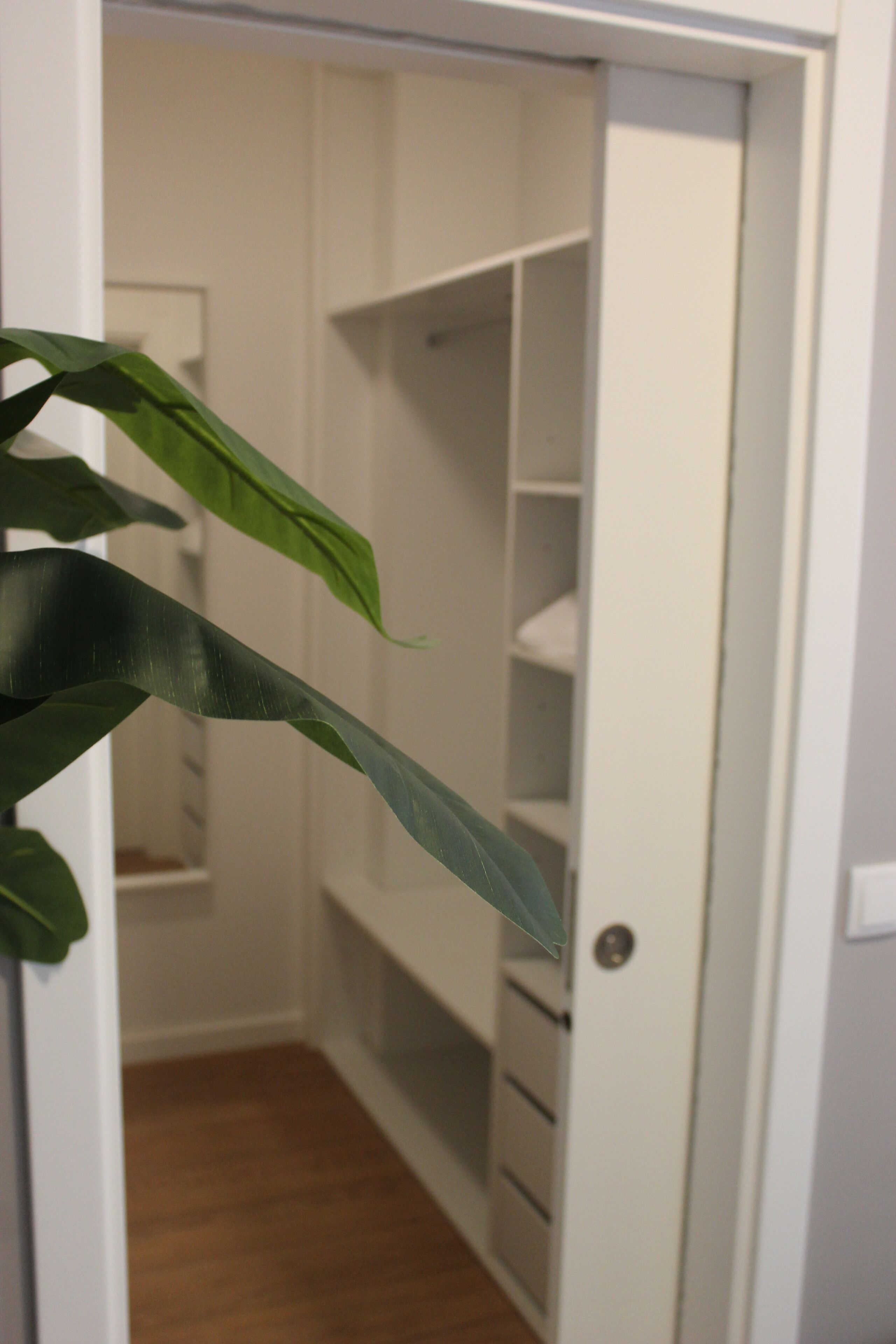 A white closet with shelves and drawers, a wooden floor, and a door with a lock.