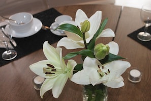 A dining table with a vase of white lilies, a candle, and a glass of water.
