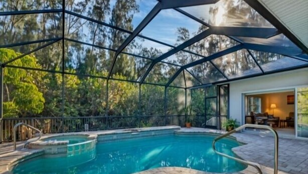 Piscina com estrutura de vidro, rodeada por um espaço de área externa com piso de pedra.