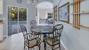 Uma sala de jantar com uma mesa redonda e cadeiras, uma luminária no teto e vista para o exterior.