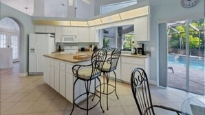 Cozinha moderna com ilha central, banquetas e vista para uma piscina.
