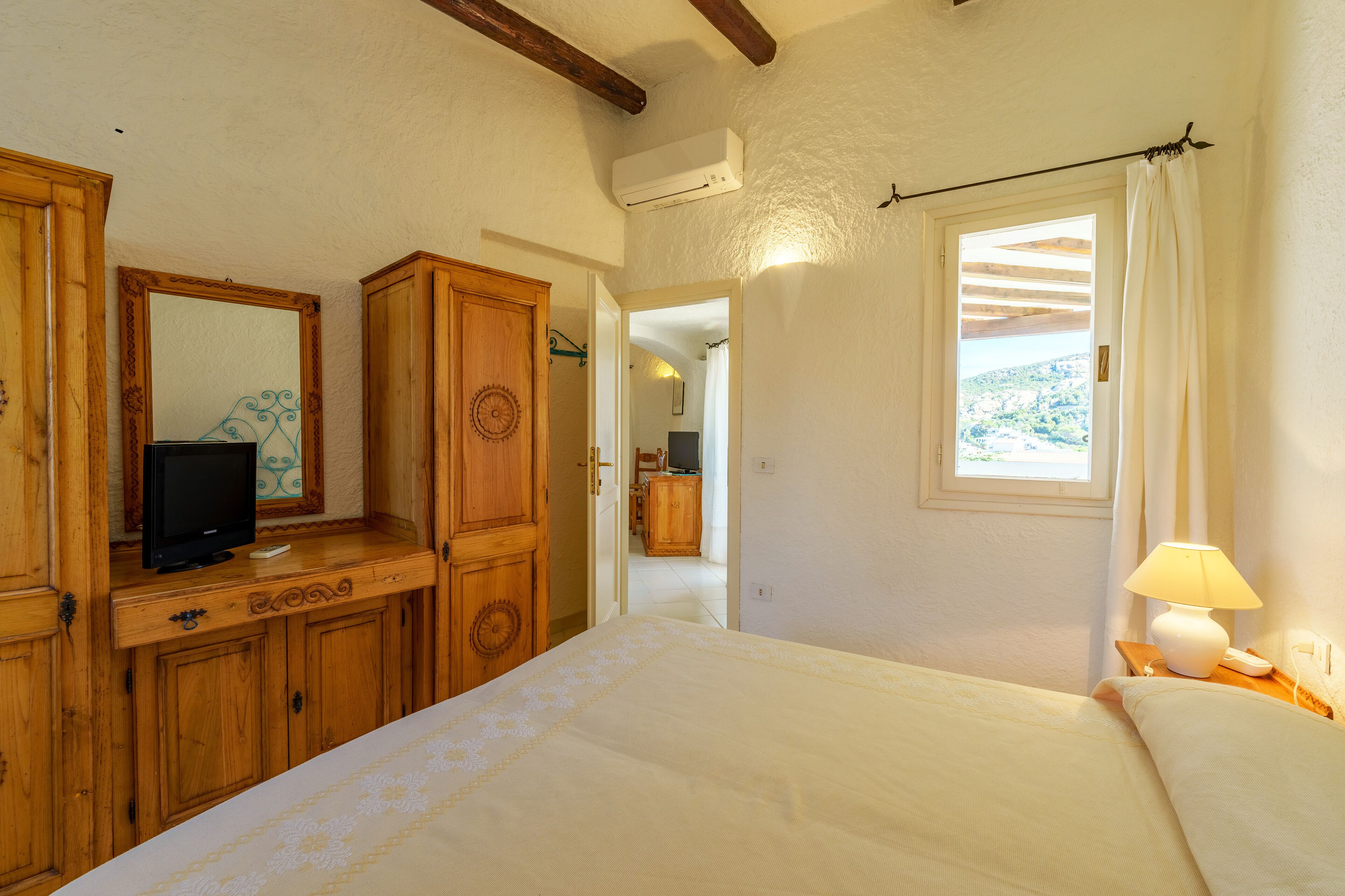 A bedroom with a bed, wooden wardrobe, a television on a dresser, and a window with curtains.