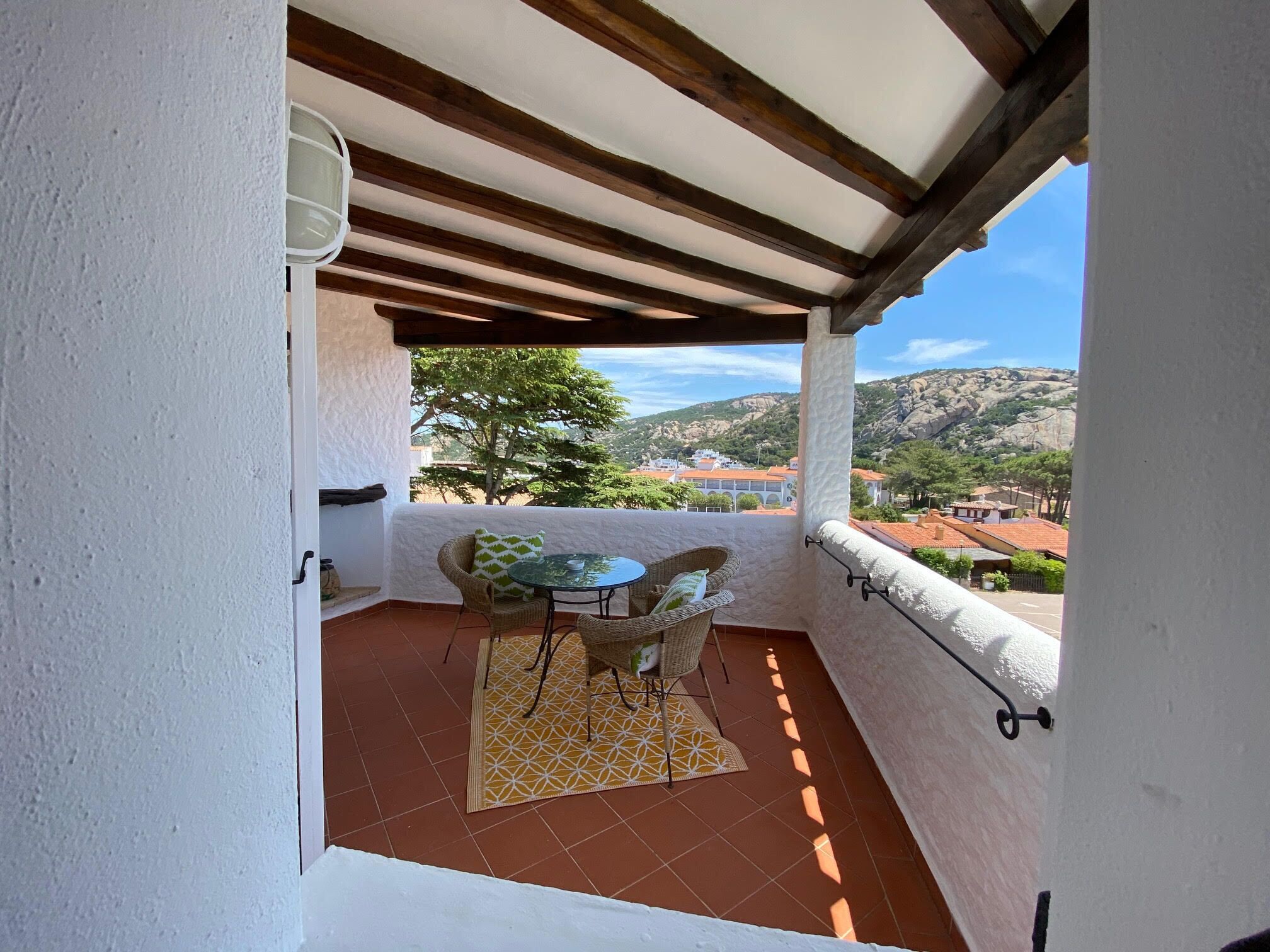 Un balcon avec une table et des chaises, un tapis à motifs et une vue sur une ville et des collines en arrière-plan.